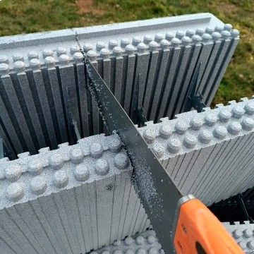 Cutter arancione taglia un blocco cassero in polistirene espanso del sistema costruttivo Bioisotherm, progettato per edifici antisismici ad alto isolamento termico e acustico. Soluzione efficiente per costruzioni eco-sostenibili e ad alte prestazioni energetiche.