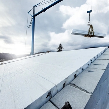 Pannelli Plastbau® New Classic di Bioisotherm in fase di installazione su un tetto. Un cielo nuvoloso fa da sfondo, mentre una gru solleva i pannelli. Ideale per costruzioni sostenibili, garantisce isolamento termico ed efficienza energetica.