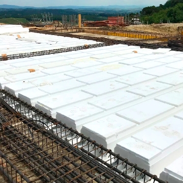 Pannelli in EPS della linea Plastbau di Bioisotherm posizionati su una struttura di armature in un cantiere edile. I pannelli, parte del sistema di costruzioni sostenibili, offrono isolamento termico e resistenza sismica. Sfondo di colline e vegetazione.