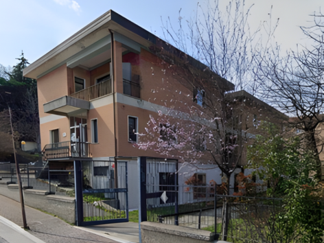 Edificio scolastico a tre piani con cappotto sismico Argisol di Bioisotherm ad Ascoli Piceno. Facciata ristrutturata visibile, circondata da alberi e strada adiacente. Miglioramento energetico e antisismico evidenziati nel contesto del progetto di adeguamento sismico.