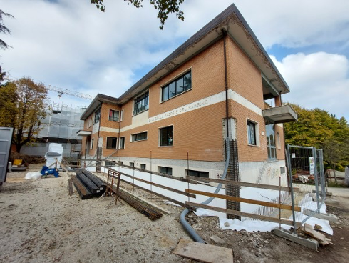 Edificio scolastico in fase di adeguamento sismico ad Ascoli Piceno, con l'applicazione del sistema a cappotto sismico Argisol e Bioisotherm. L'immagine mostra lavori in corso con impalcature e materiali da costruzione attorno alla struttura in mattoni.